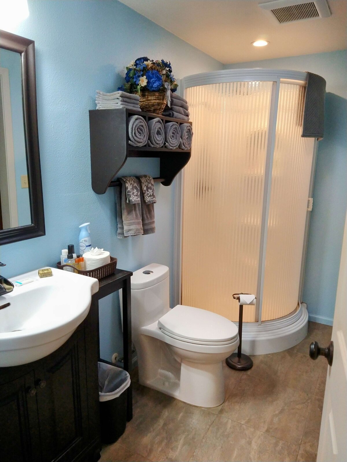 Bathroom with sink, shower, and toilet is stocked with towels.