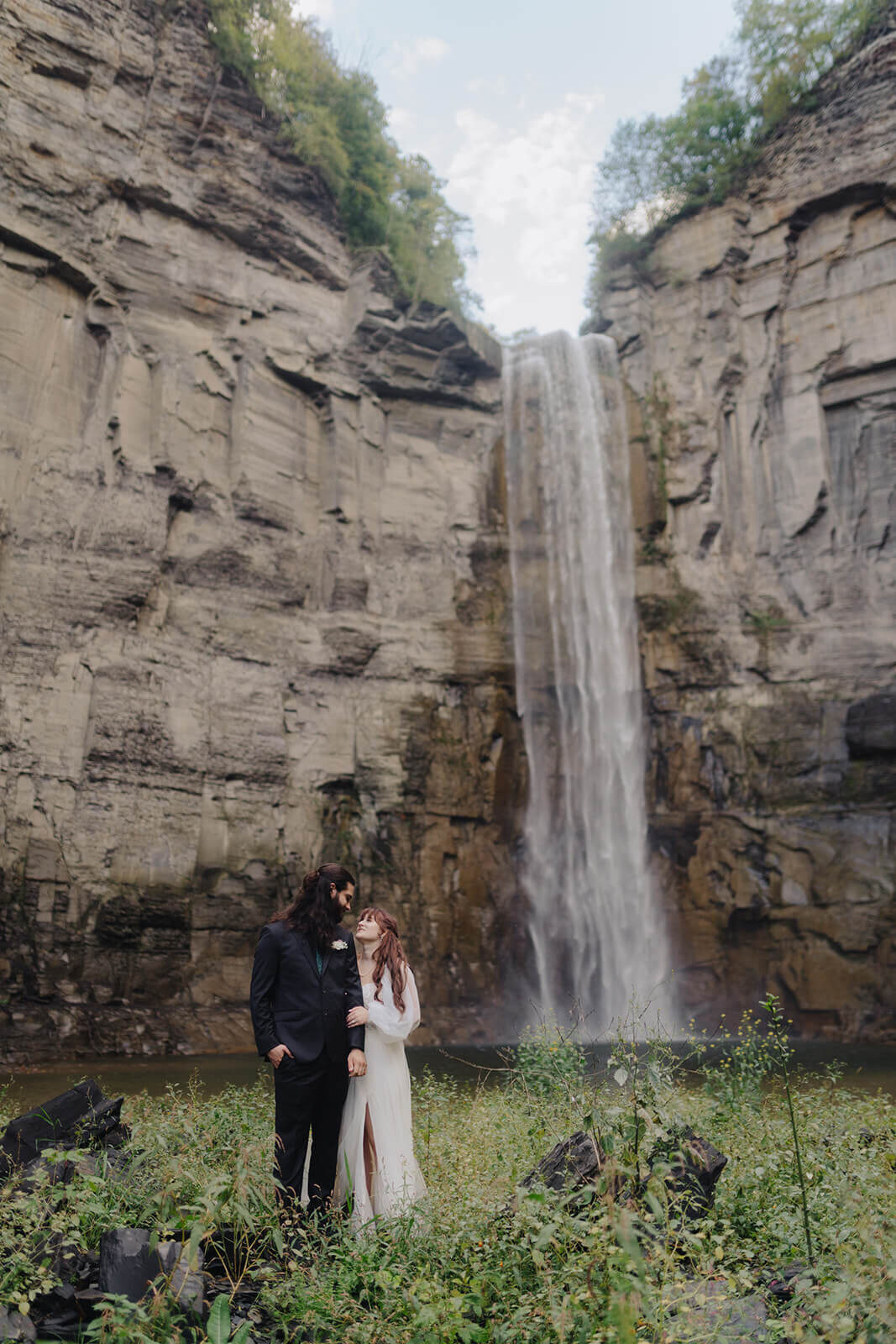 Bride and groom standing in front of waterfall at Finger Lakes wedding, NY