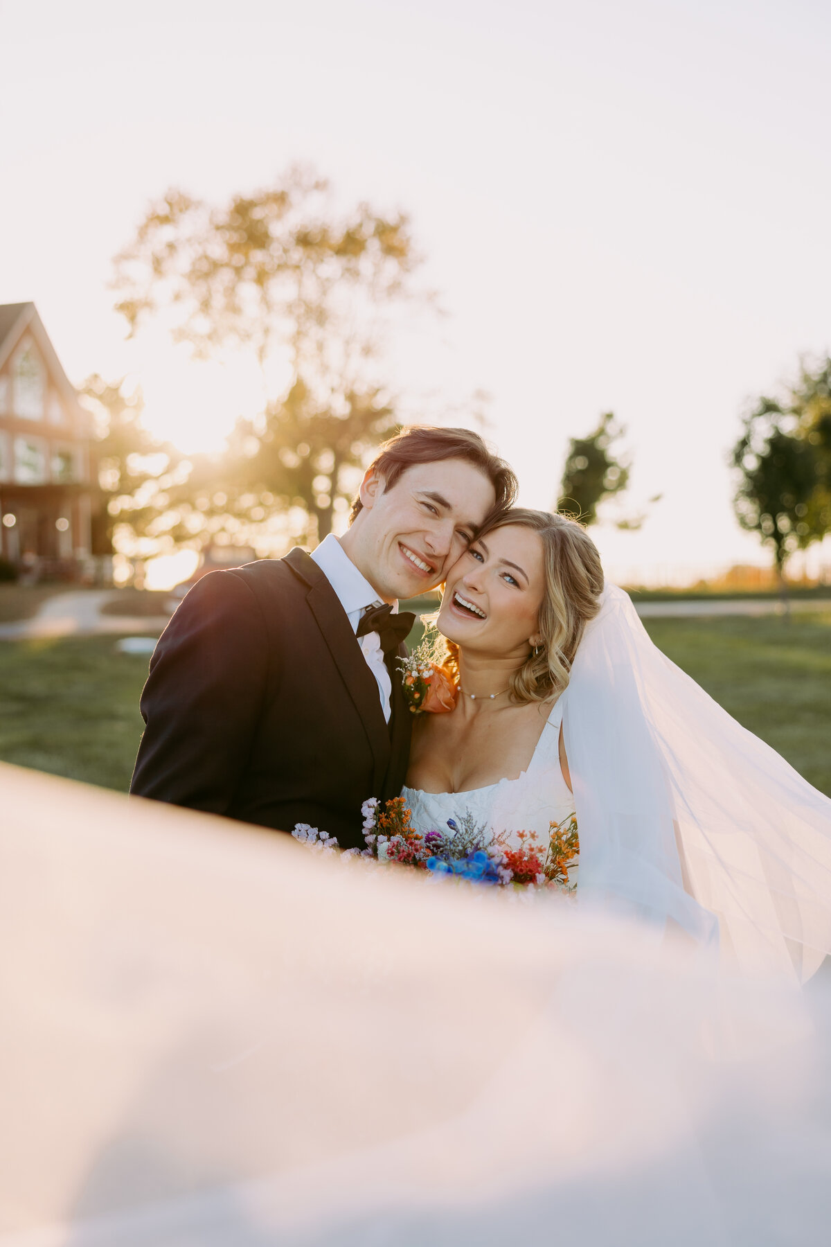 Photo shows bride and groom during sunset at Willow Creek Barn in Indiana. The veil is swooped in front of the camera.