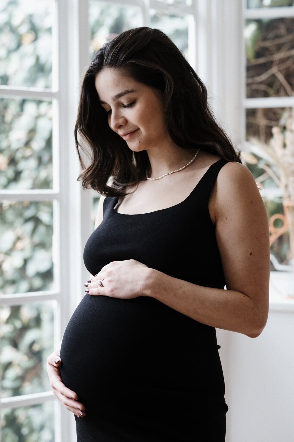 Woman in black dress with pearl necklace holds her pregnant belly