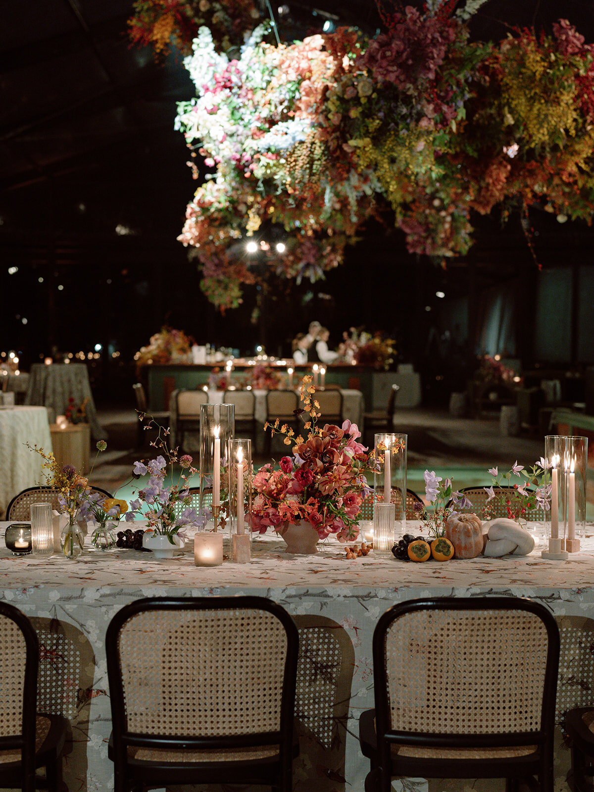 Clustered and styled floral arrangements, fruits, and art pieces for fall wedding reception. Low centerpieces mixed with ikebana arrangements and bud vases decorate the reception tables at this fall wedding. Floral centerpieces featuring orchids, ranunculus, sweet peas, and bittersweet. Styled wedding tables with fruits, curated candles, and floral arrangements. Tasteful fall color palette of copper, ruby, gold, burgundy, rust, and lavender. Design by Rosemary & Finch Floral Design in Nashville, TN.