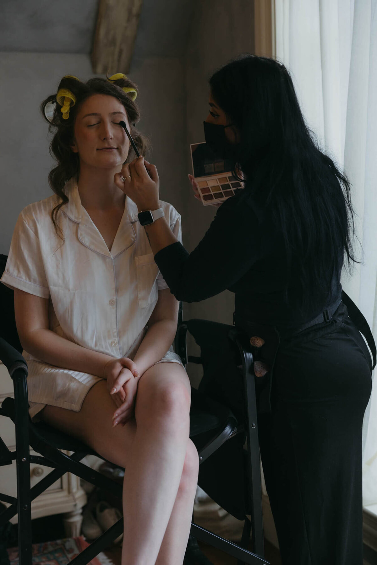 A bride gets her makeup done at a wedding planned by Birdie June Events & Rentals. 