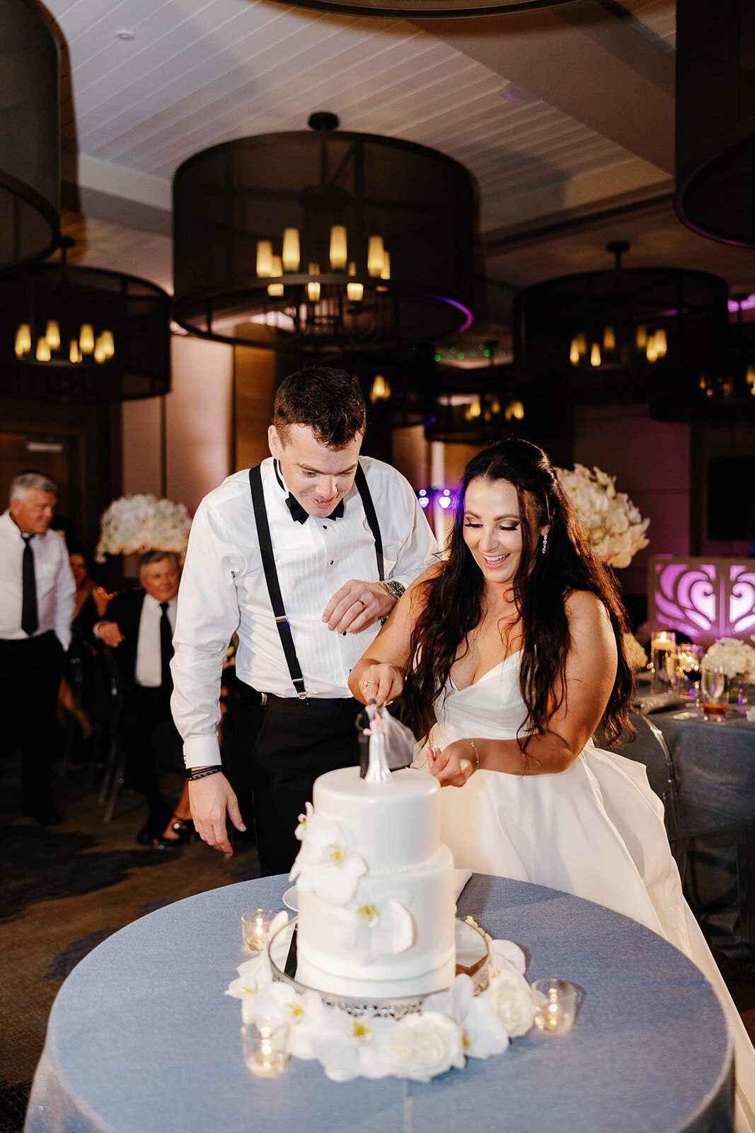 Ashley and Cameron share a joyous moment as they cut their elegant white wedding cake adorned with fresh orchids at Ocean Reef, Key Largo.