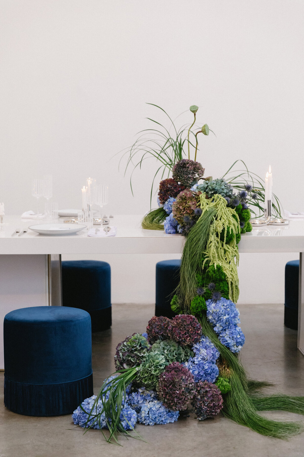 Modern wedding reception table featuring cascading blue hydrangeas, greenery, and tall sculptural florals at a New York City studio.