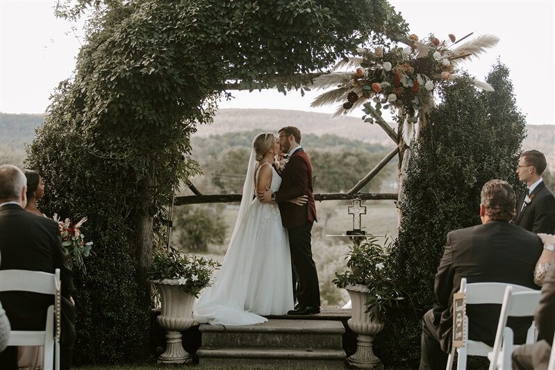 Bride and groom kissing under the floral arch