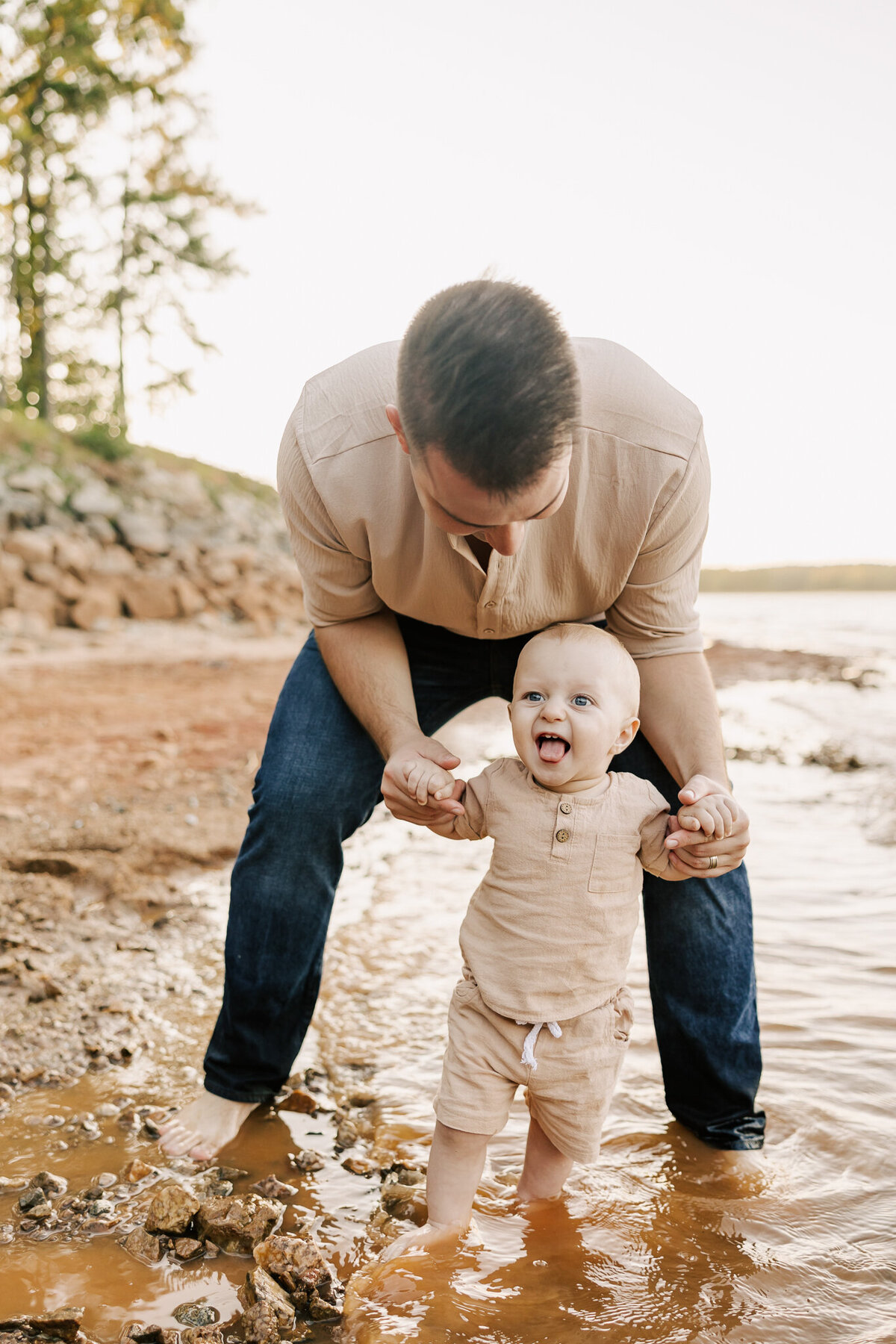 dad holding the hands of his 9-month old baby boy while they stand in the water at clarks hill lake