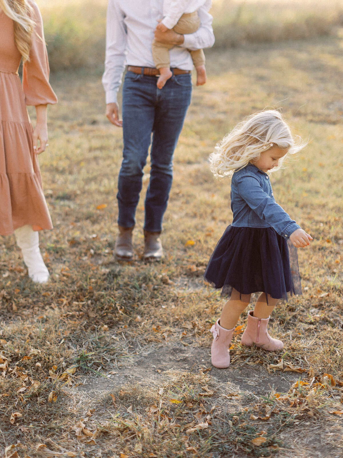 toddler girl twirls frilly skirt while family walks behind her