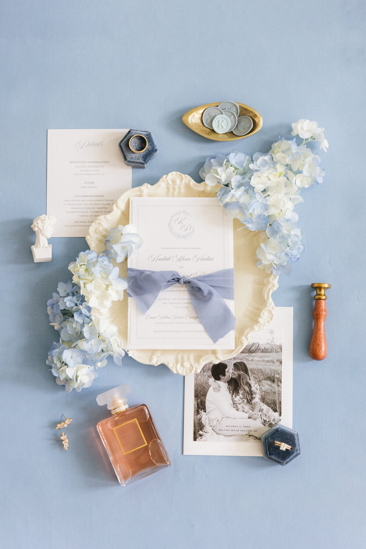 Elegant Hilton Head Island wedding invitation flat-lay with blue hydrangeas, velvet ring box, wax seals, and Chanel perfume—captured by luxury wedding photographer Amia Marcell.