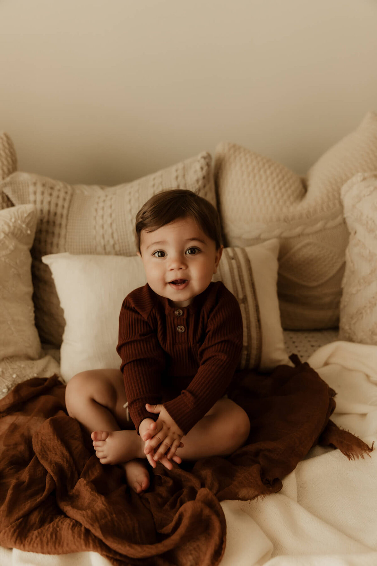 Baby clapping and smiling on a bed while sitting down.