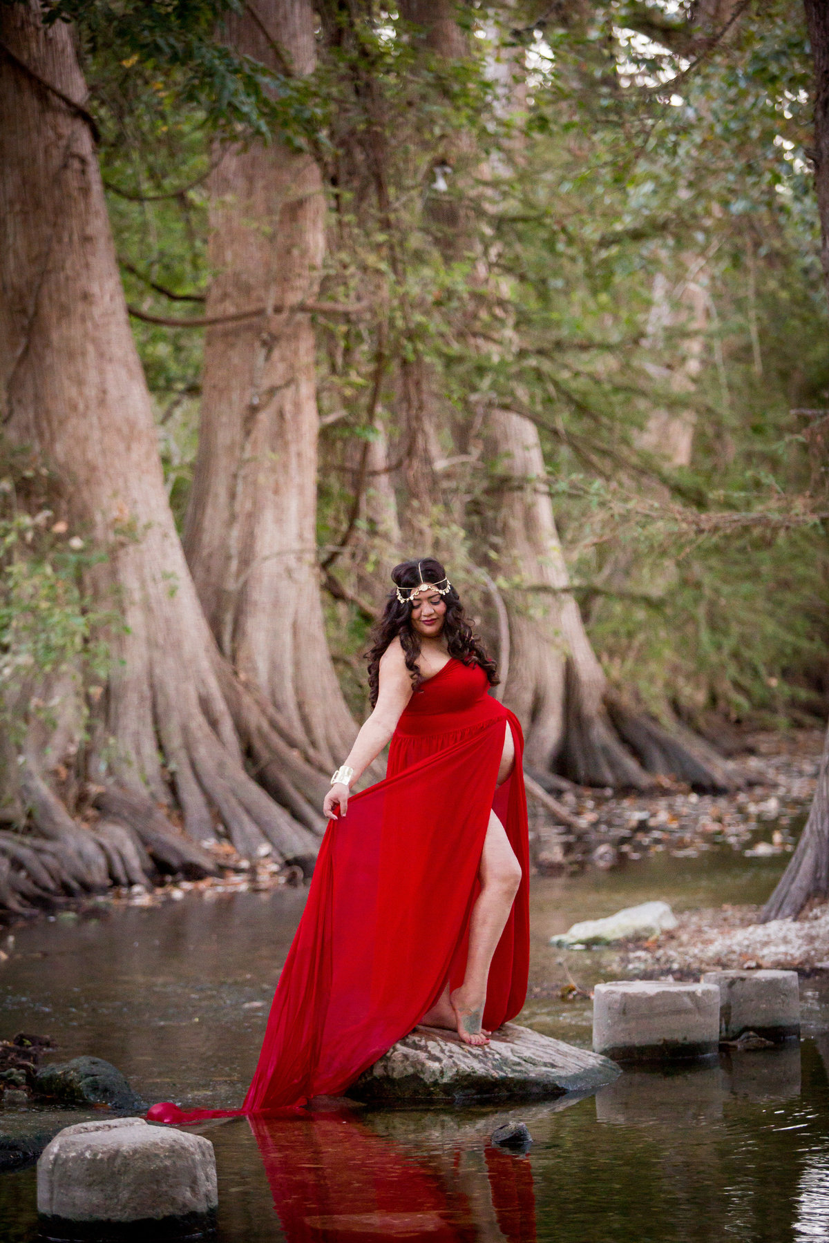 pregnant woman standing on a rock in a river wearing a red maternity dress in Cibolo Nature Center