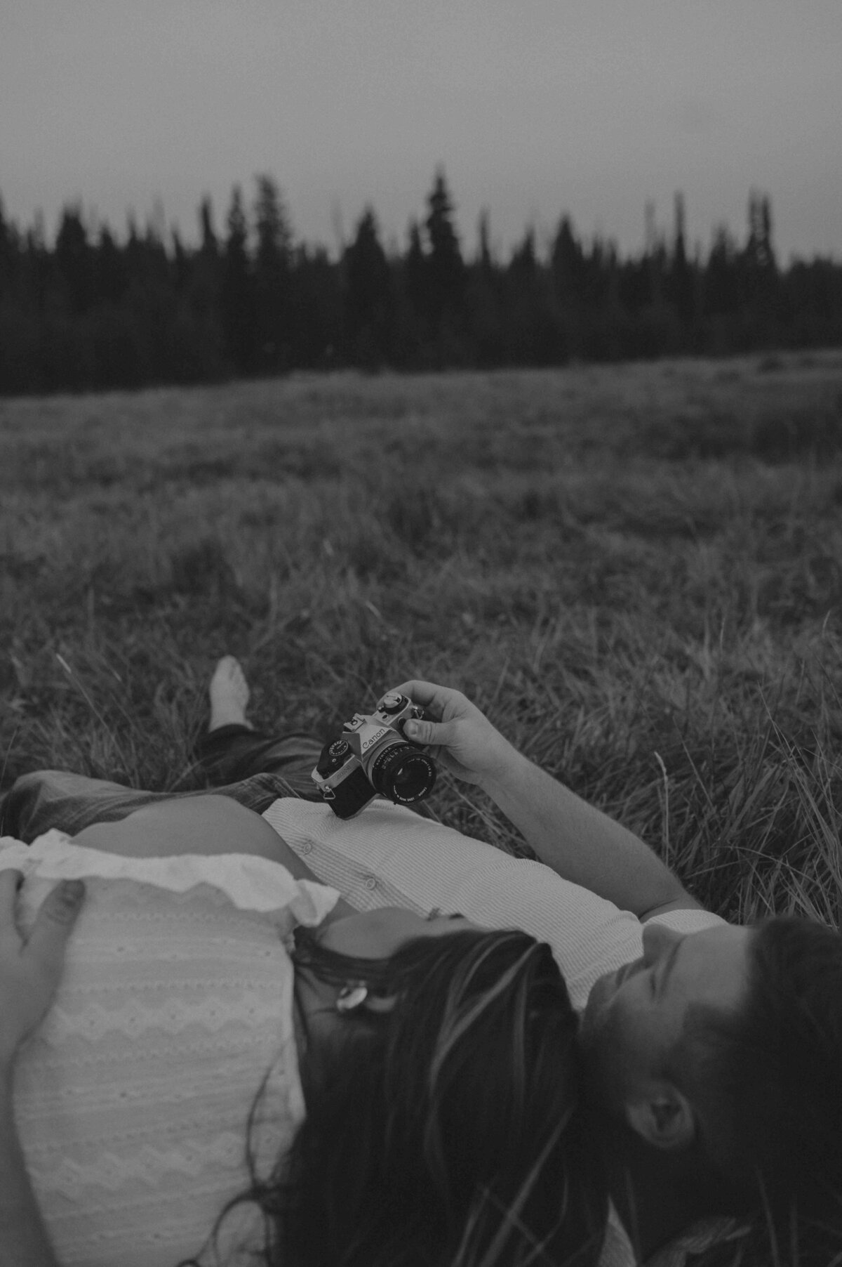 girl leans her head on guys chest and they lay in a field 