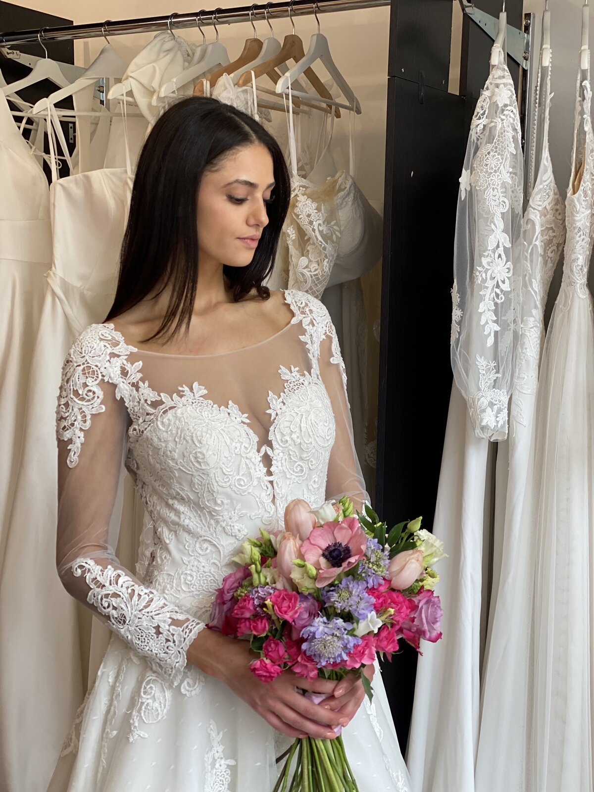 A bride in a beautiful bridal store holding a colorful bouquet in a modest and modern white a-line wedding gown with lace details.