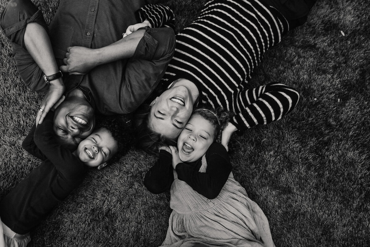 Black and white joyful lifestyle family portrait. Mixed race family lying on the grass smiling and laughing