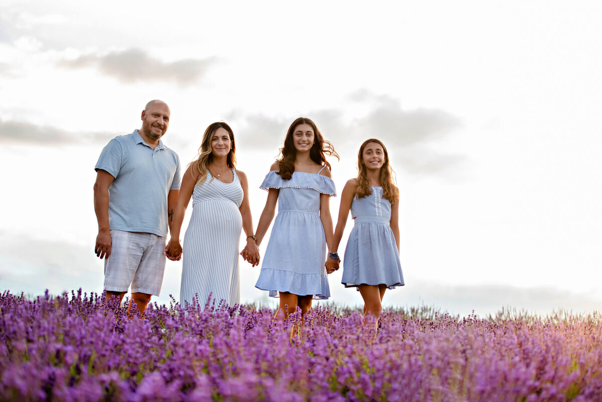 mom and dad holding their teenage daughters hands with the sun-setting behind them in a lavender field for their outdoor maternity photography session in Burlington, On