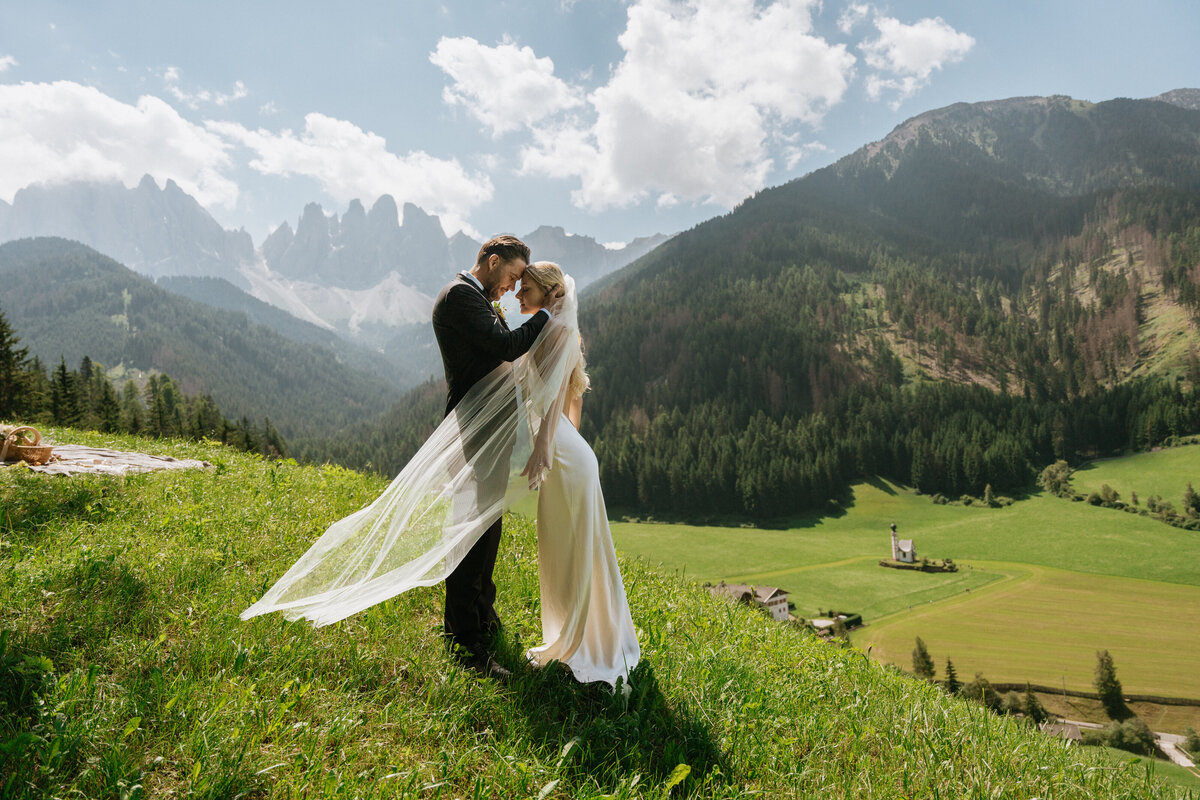 Couple standing together kissing in alpine field in Dolomites