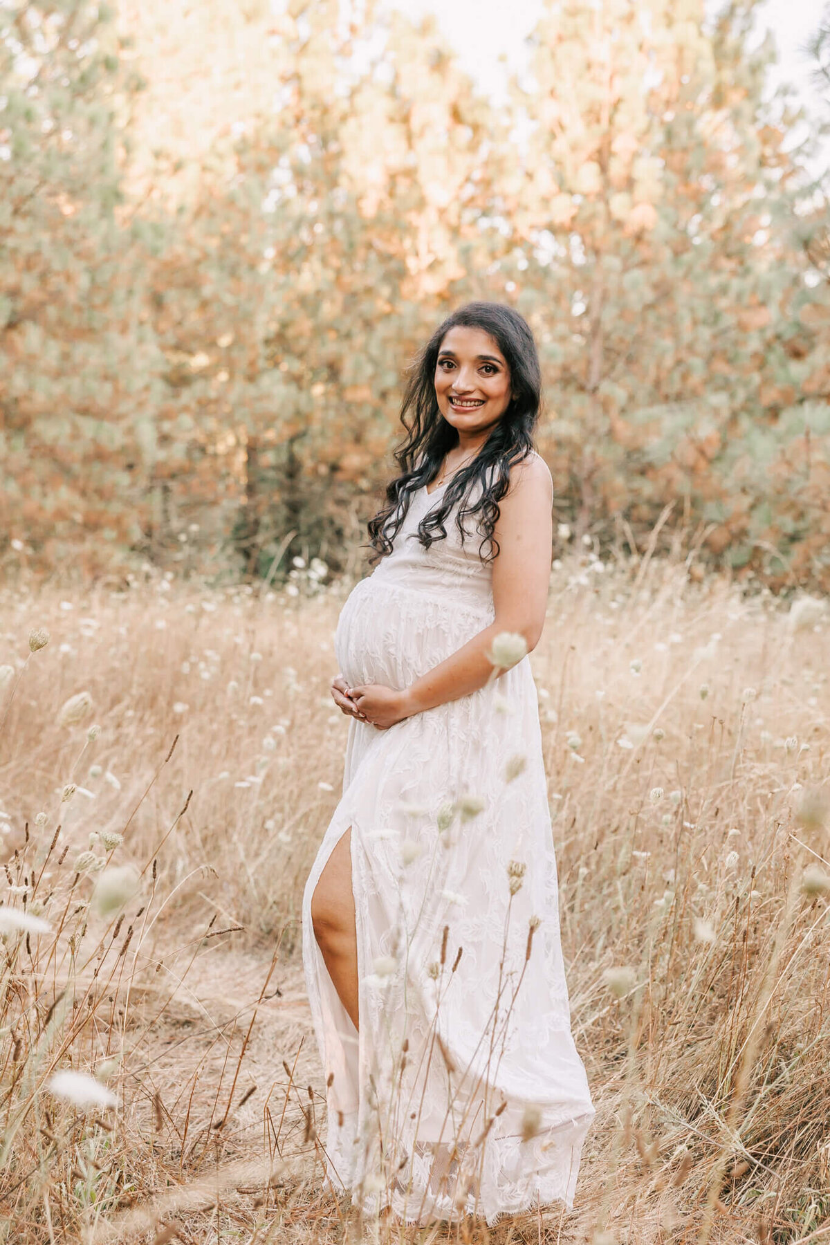 portrait of woman smiling at camera in beaverton oregon maternity portrait. she is wearing a white dress.