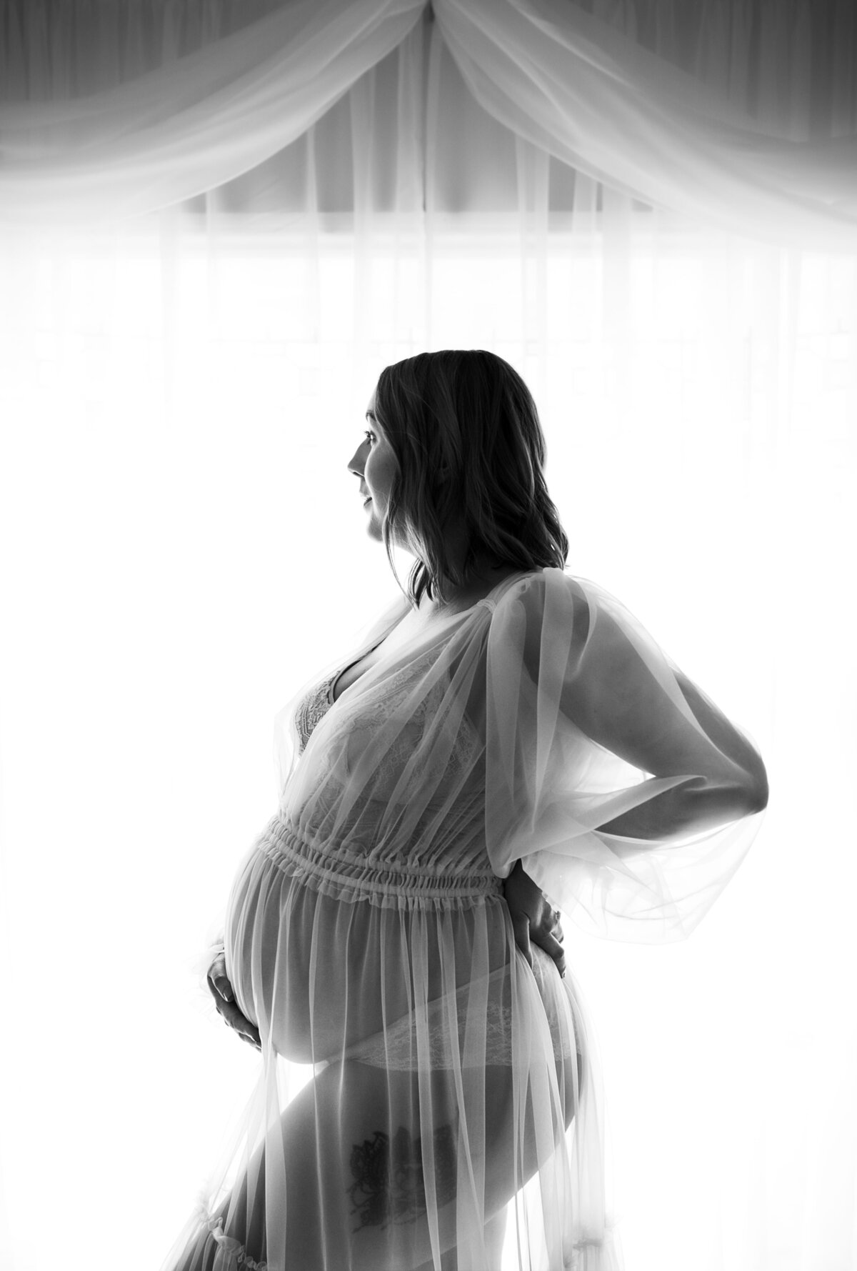 Black and white backlit photo of a pregnant woman in a sheer dress