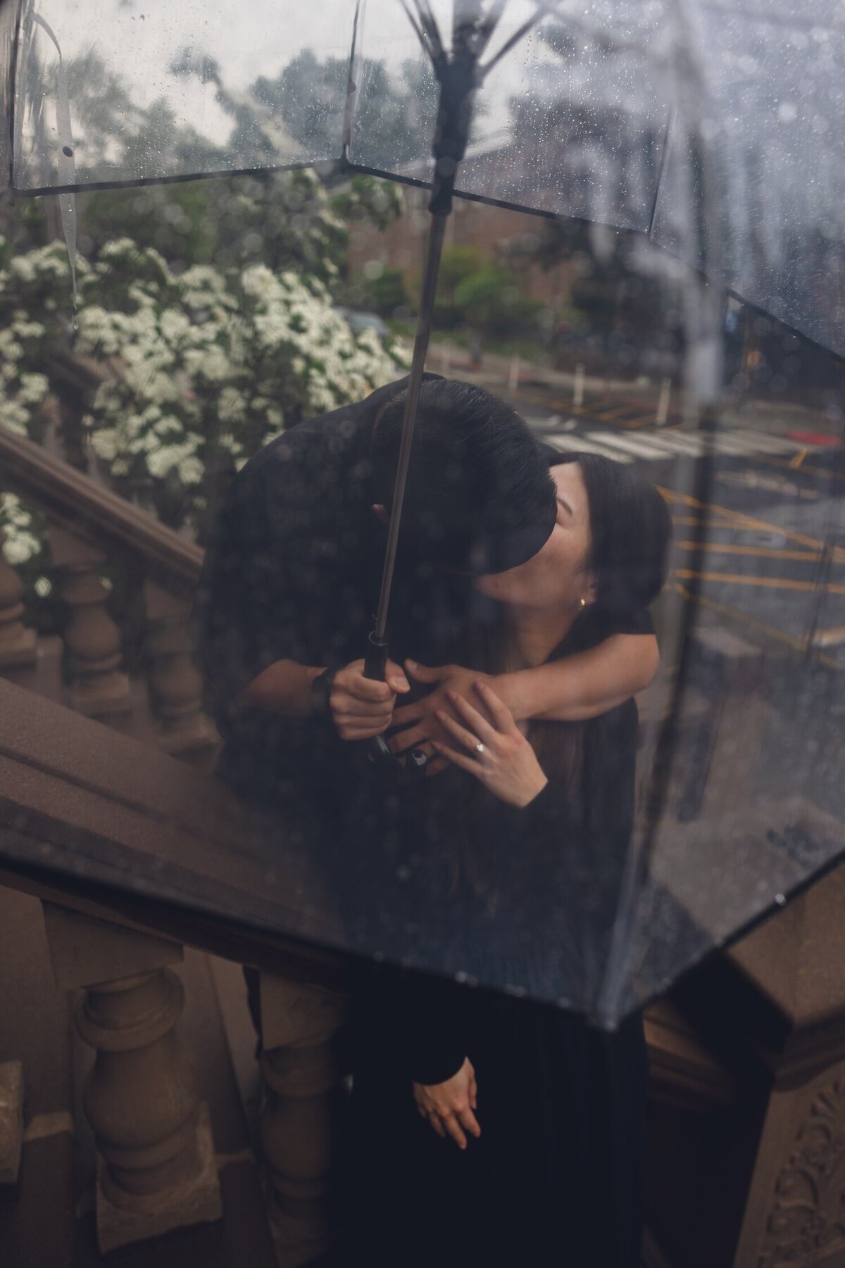 Couple kissing on rainy brownstone steps with umbrella