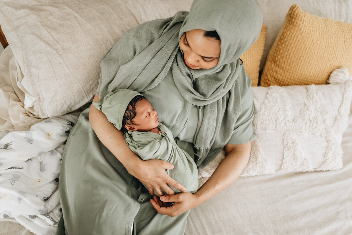 Newborn photography of mother holding newborn babe in bed.