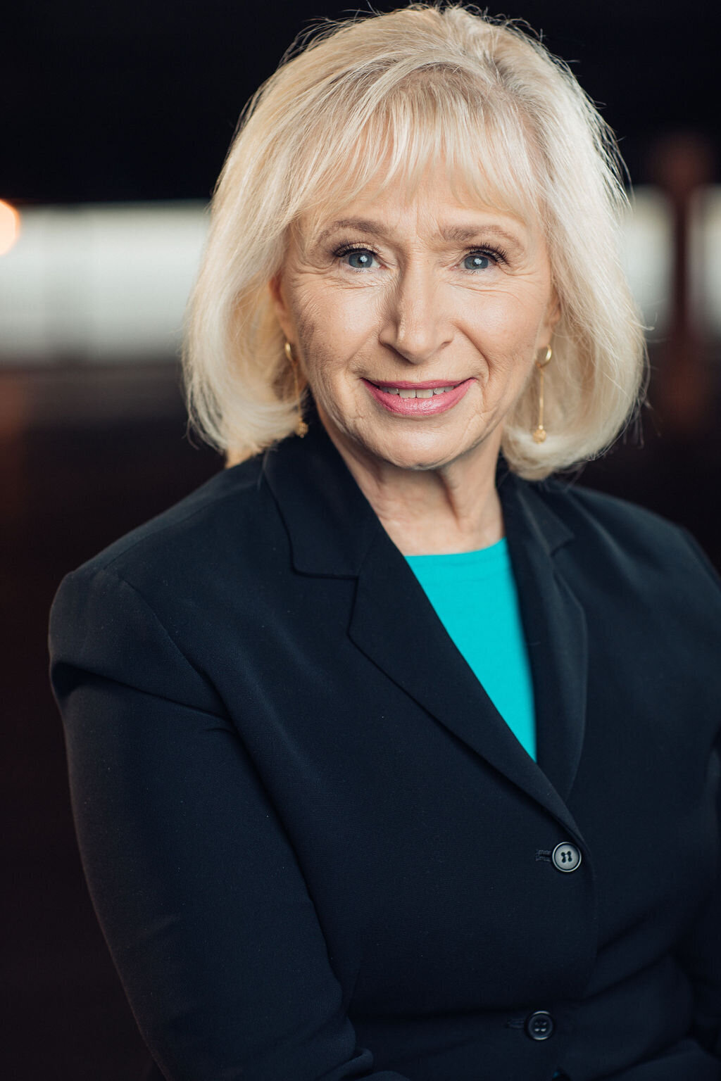 Headshot Photograph Of Woman In Outer Black Blazer And Inner Blue Shirt