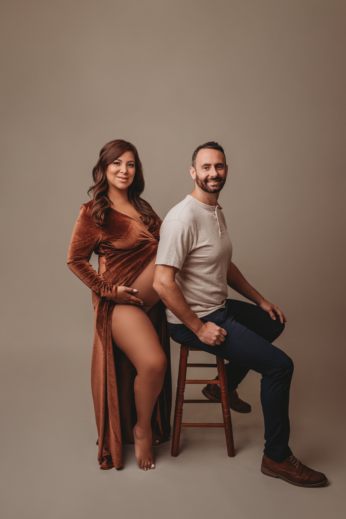 Pregnant woman at maternity and newborn studio of Atlanta posing for maternity portrait wearing copper velvet maternity gown standing with husband