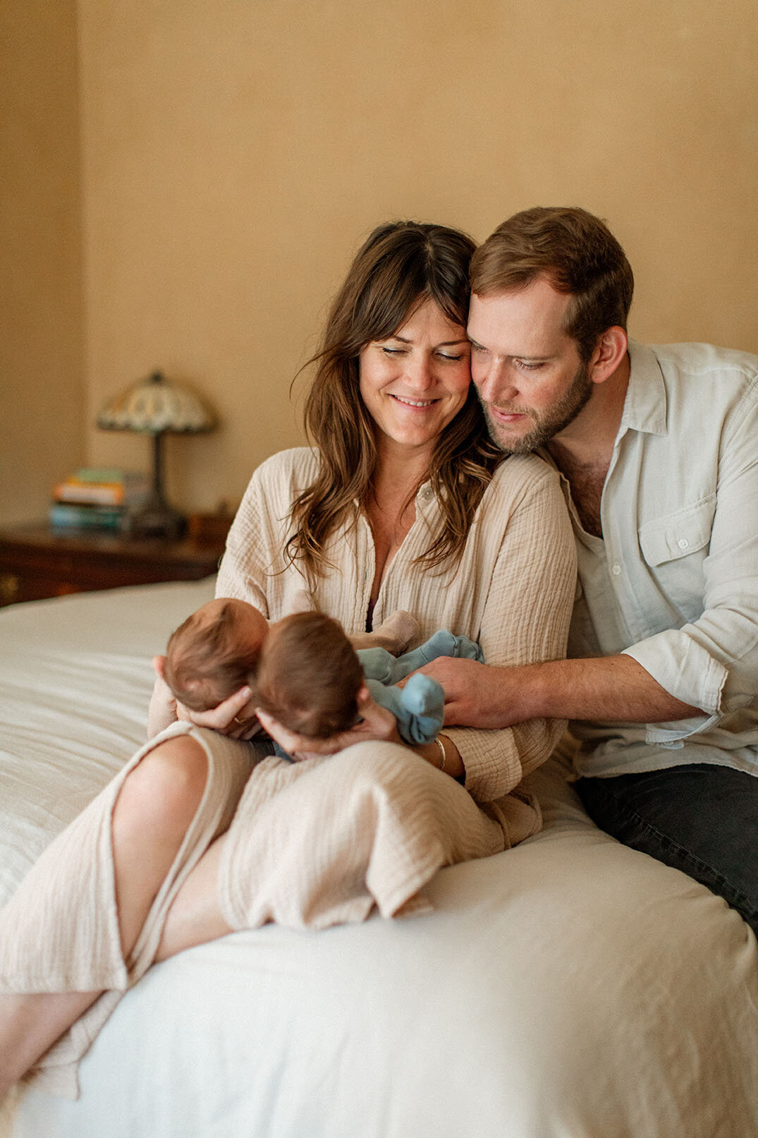 Twin newborns with parents on bed during family session - Sara James captures special twin birth celebrations and double blessing moments during intimate newborn photography in comfortable San Antonio home settings