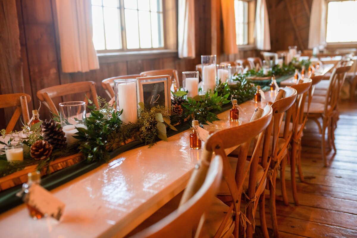 Rustic winter table setting with long wooden birch runners, candles, wintry greens and maple syrup favors.