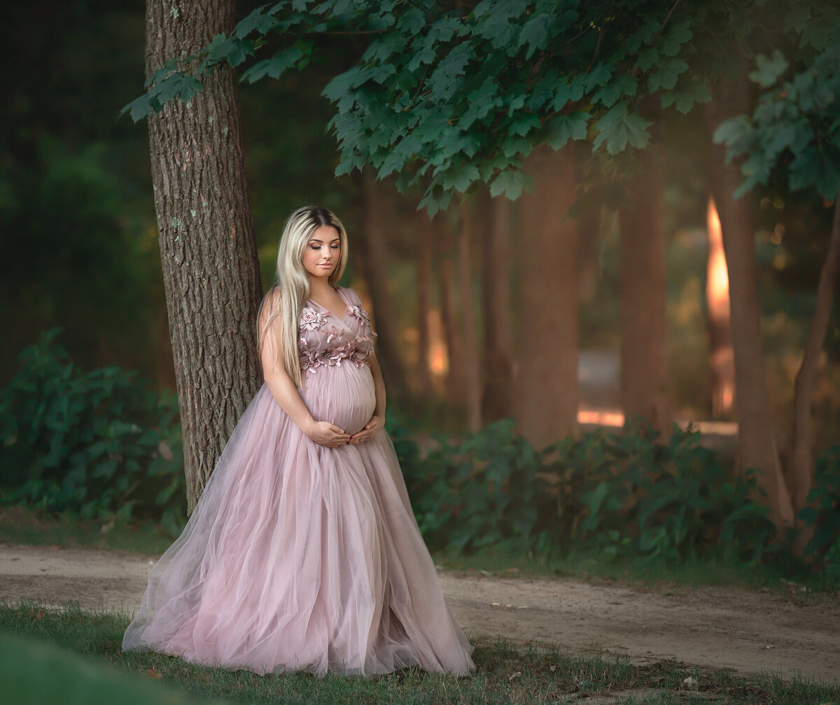 "Expecting mom-to-be leaning against a tree, bathed in golden light, during an outdoor maternity session in Ottawa"