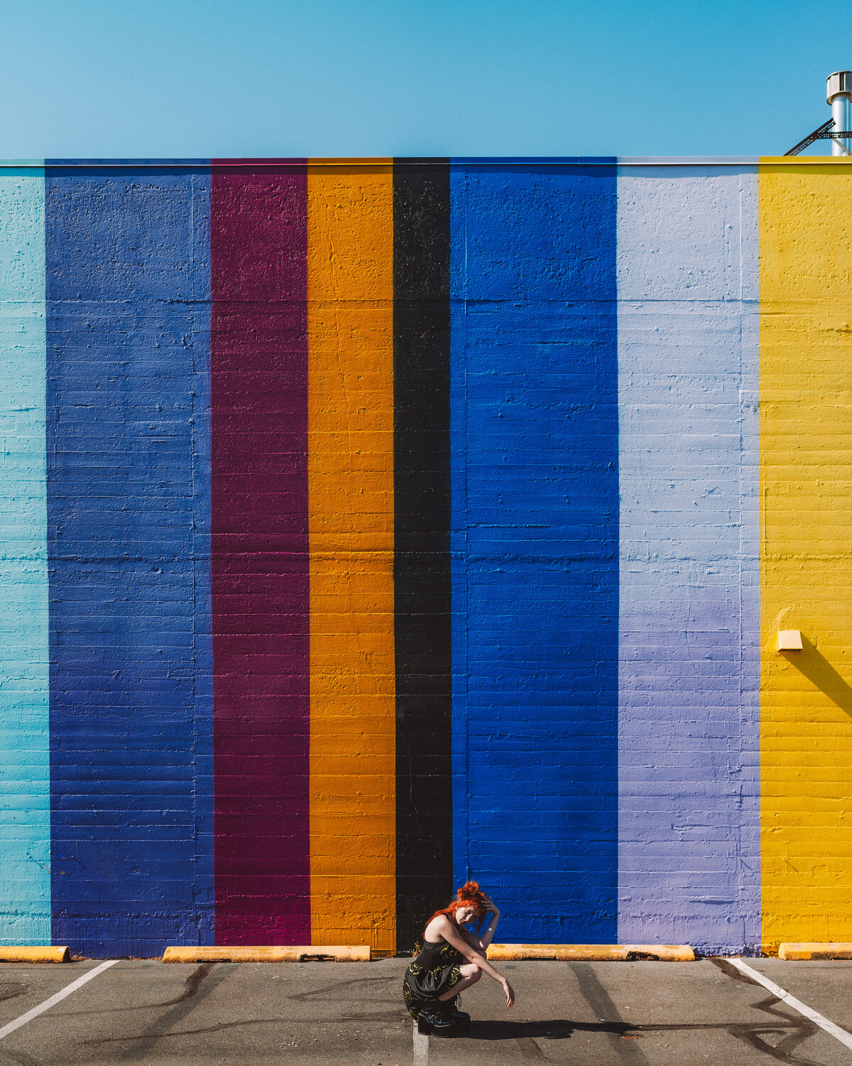 Photographer crouched in front of a bold striped mural – creative branding session by Mewphotovideo