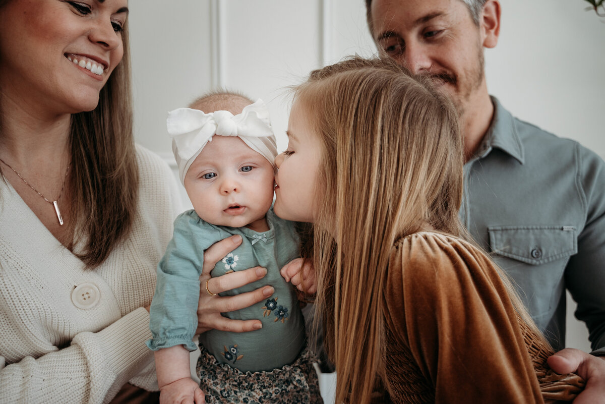 Big siste kissing small sister during a studio family photoshoot in Bartlett, IL