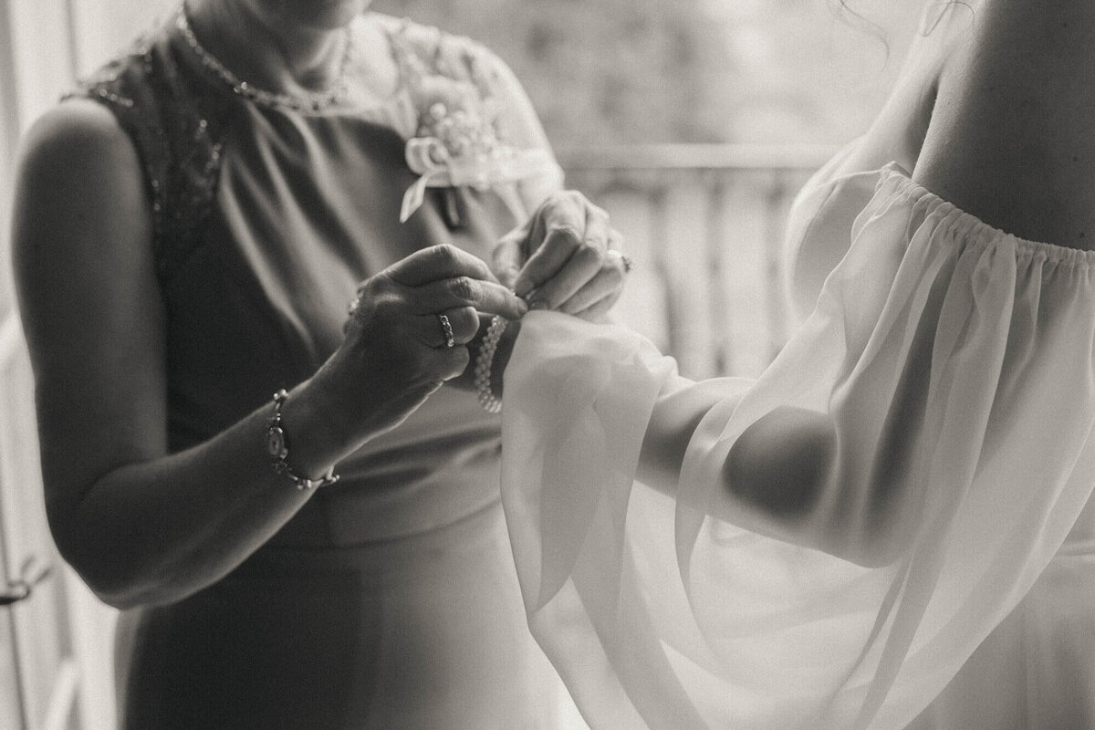 Close up of a mom buttoning the sleeve of the bride's dress. 