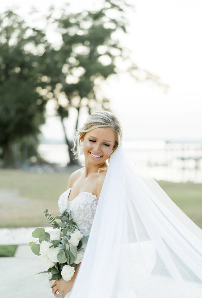 bride smiling as veil flows while holding a flower bouquet