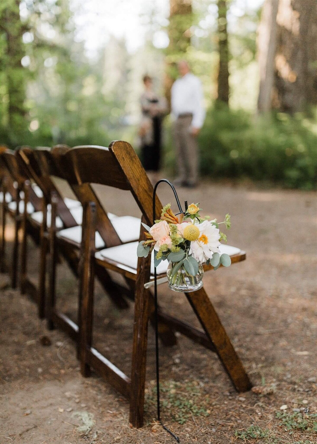 A small floral arrangement lines the aisle at outdoor summer wedding.