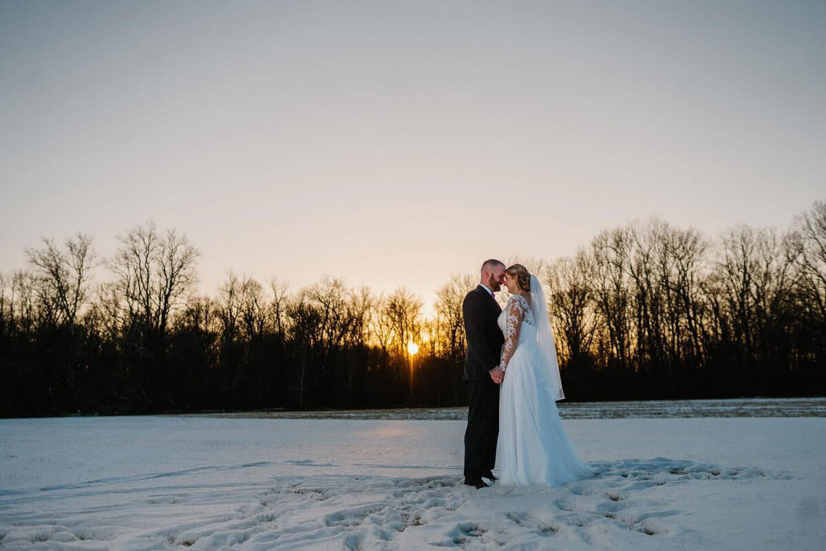 Bride and groom standing in the snow, sharing an intimate moment at sunset