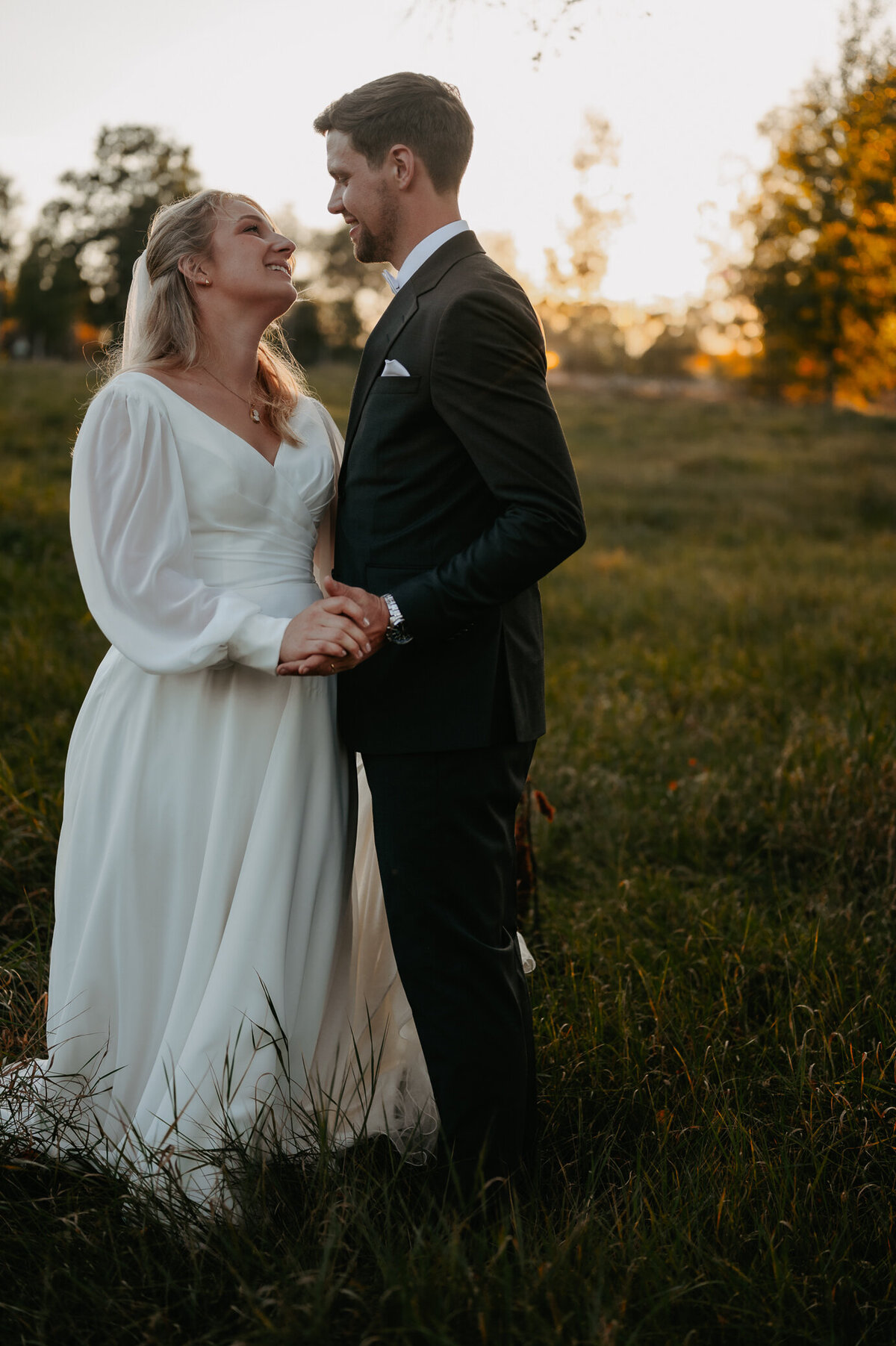 Brudpar står på ängen och hållar om varandra.