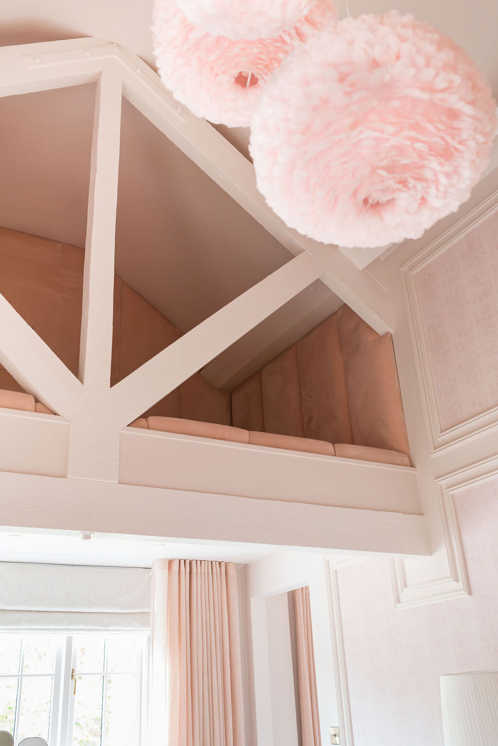 A cozy bedroom with pastel pink decor features a loft with wooden beams overhead.