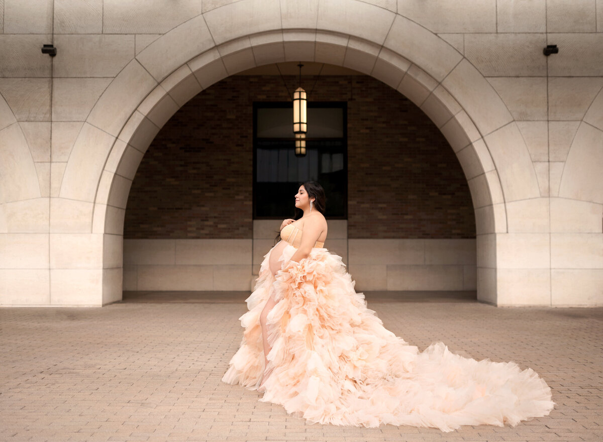 pregnant woman wearing a fluffy peach tulle dress in an archway