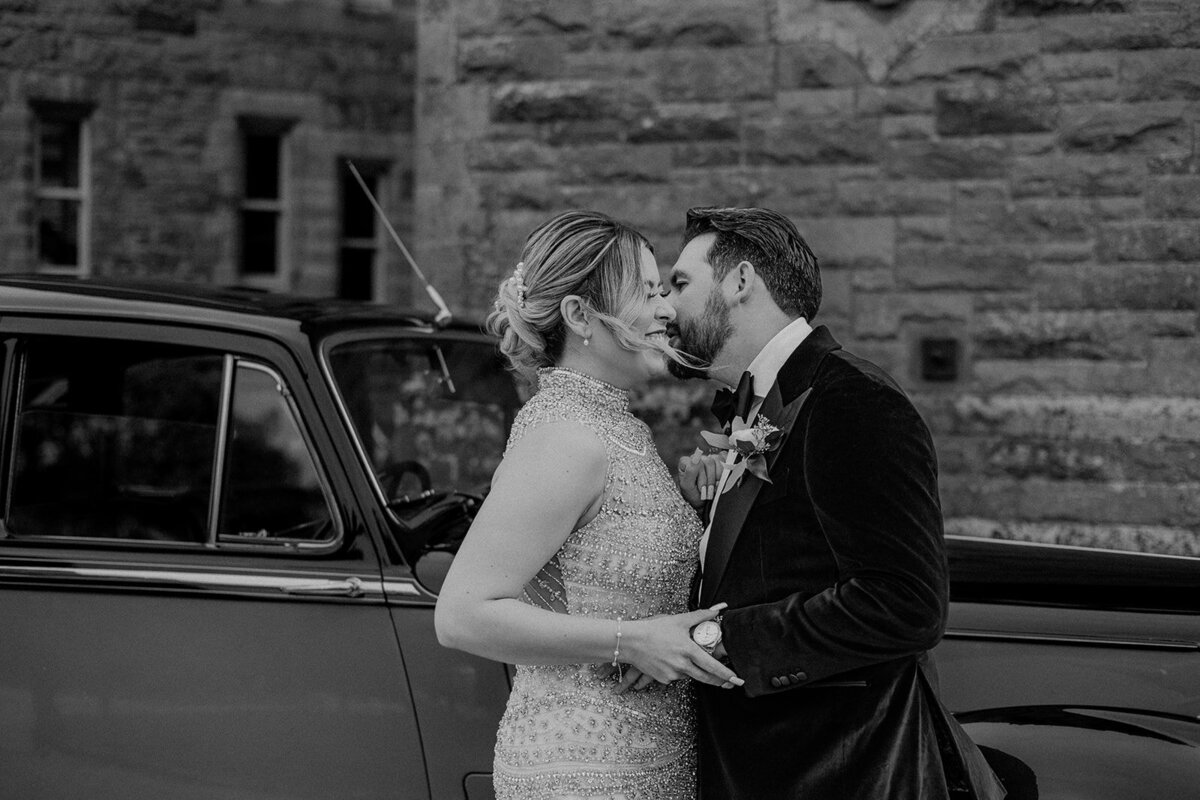 Bride and groom laughing holding each other in front of car