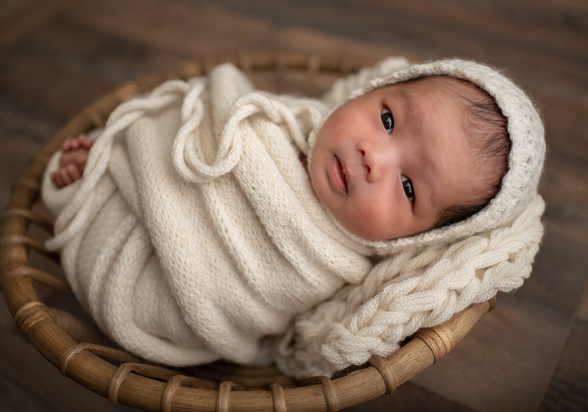 baby wrapped and laying in a bowl with a white bonnet at newborn session