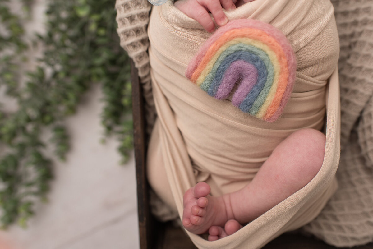 Close up of newborn boy holding a rainbow, wrapped in a tan blanket