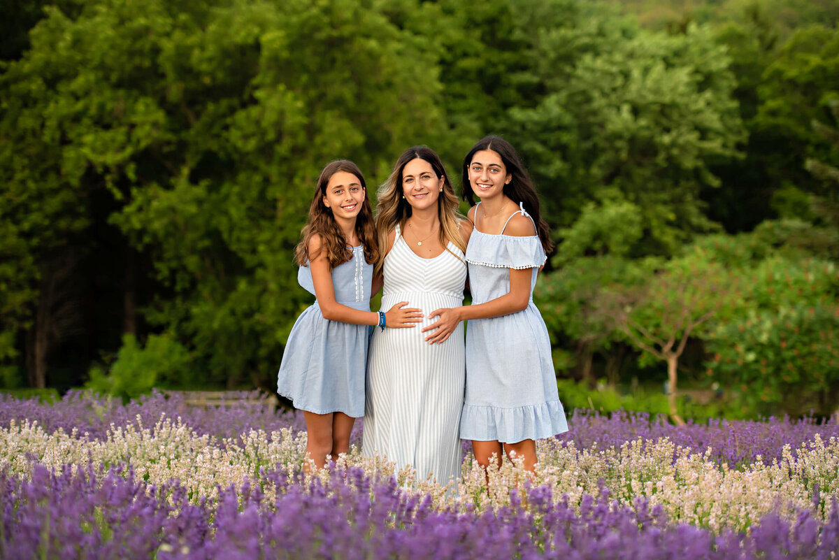 Pregnant mom standing with her two teenage daughter in a lavender field for their outdoor maternity photography session
