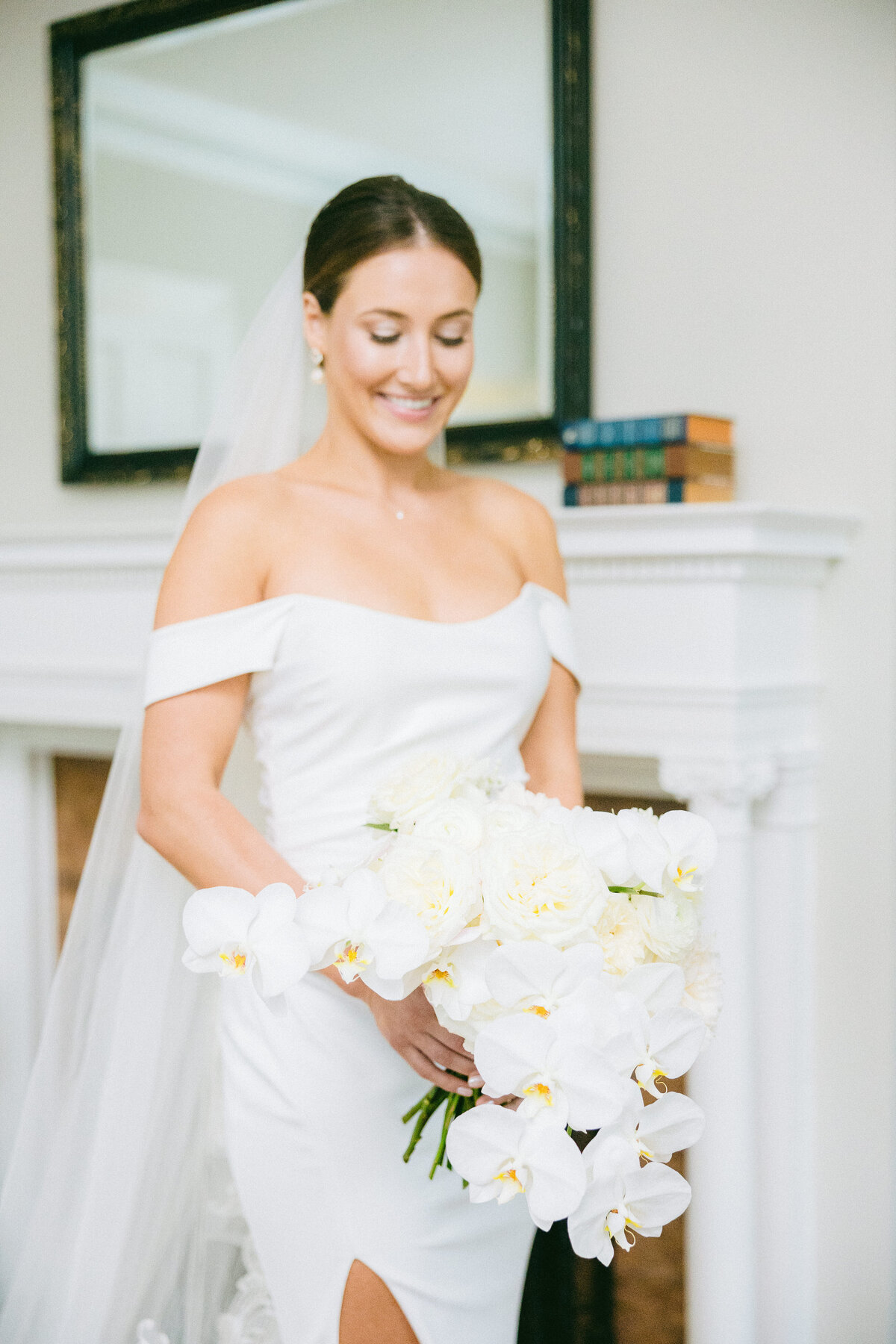 A radiant bride in a sleek off-the-shoulder wedding gown holds a luxurious bouquet of white orchids and roses at a Jekyll Island, SC wedding. Capturing timeless elegance and joy. Wedding Photographer South Carolina, Hilton Head.