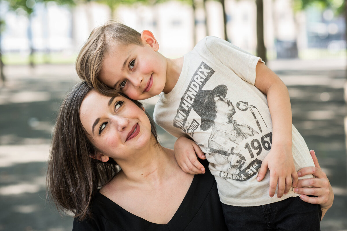 A mom smiling as her son rests his head on hers