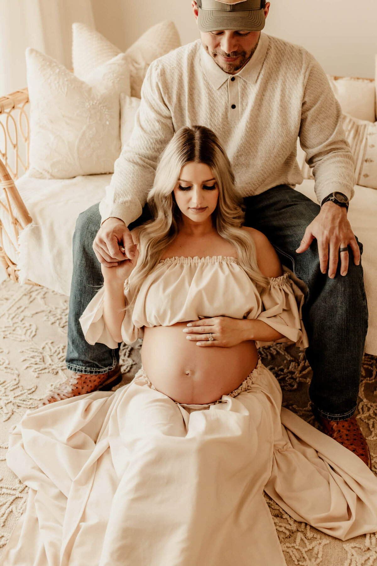 Father and mother hold hands while sitting down and looking down at expecting mother's belly.