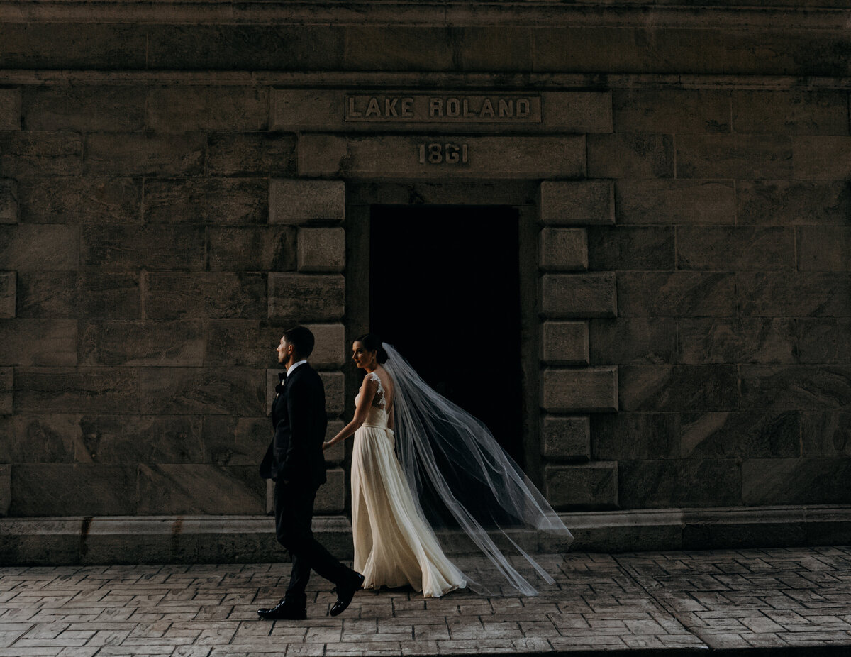 Bride and groom walk down a brick-paved street in moody natural light.