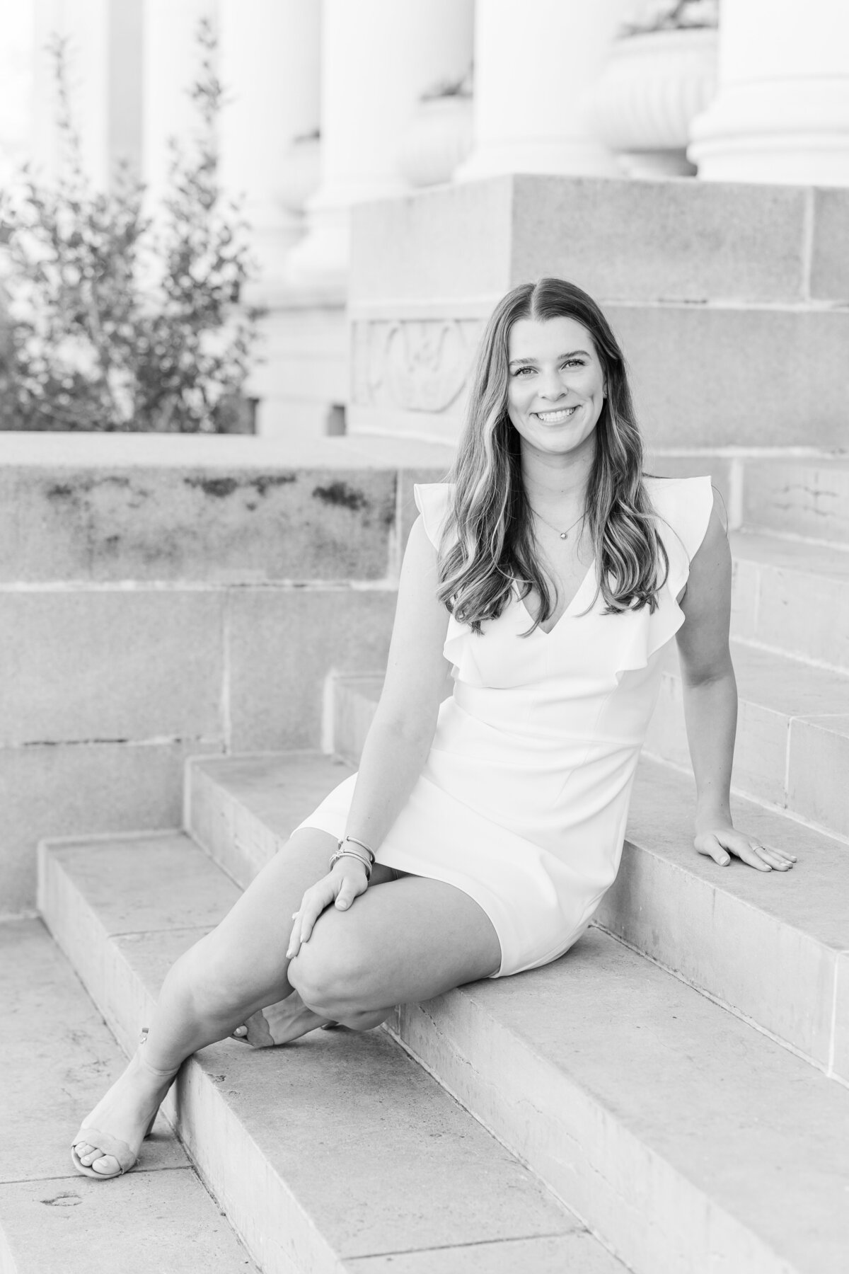 Black and white photo of a Texas A&M graduate sitting on the steps in a classic white dress, taken in College Station.
