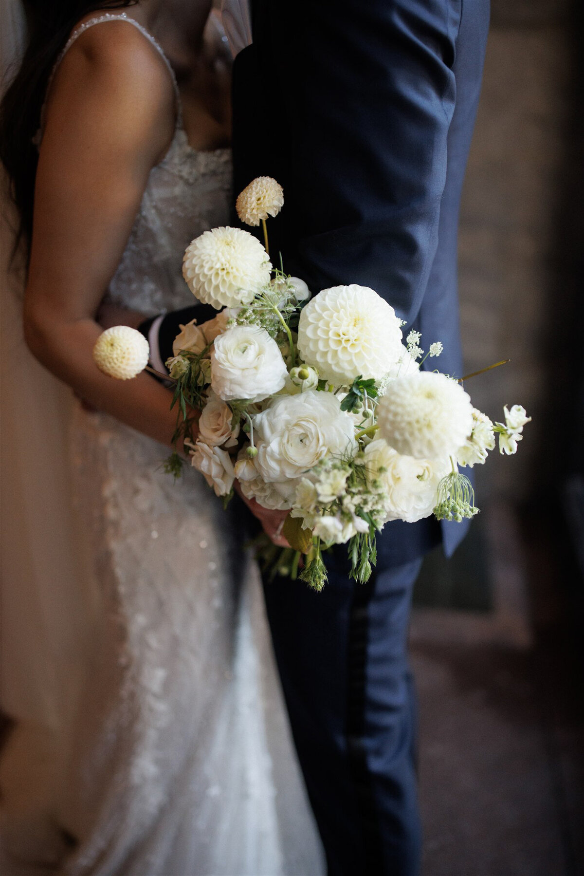 A bride and groom embrace while holding a large, elegant bouquet of white flowers.