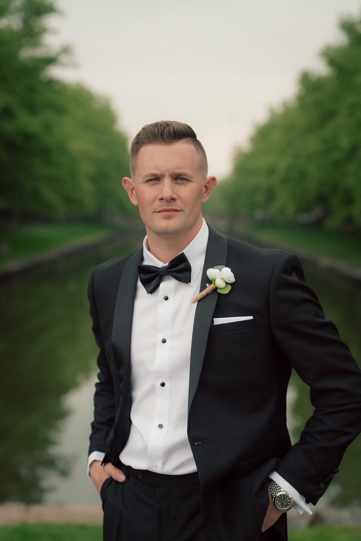 Groom solo portrait outdoors by canal in tuxedo