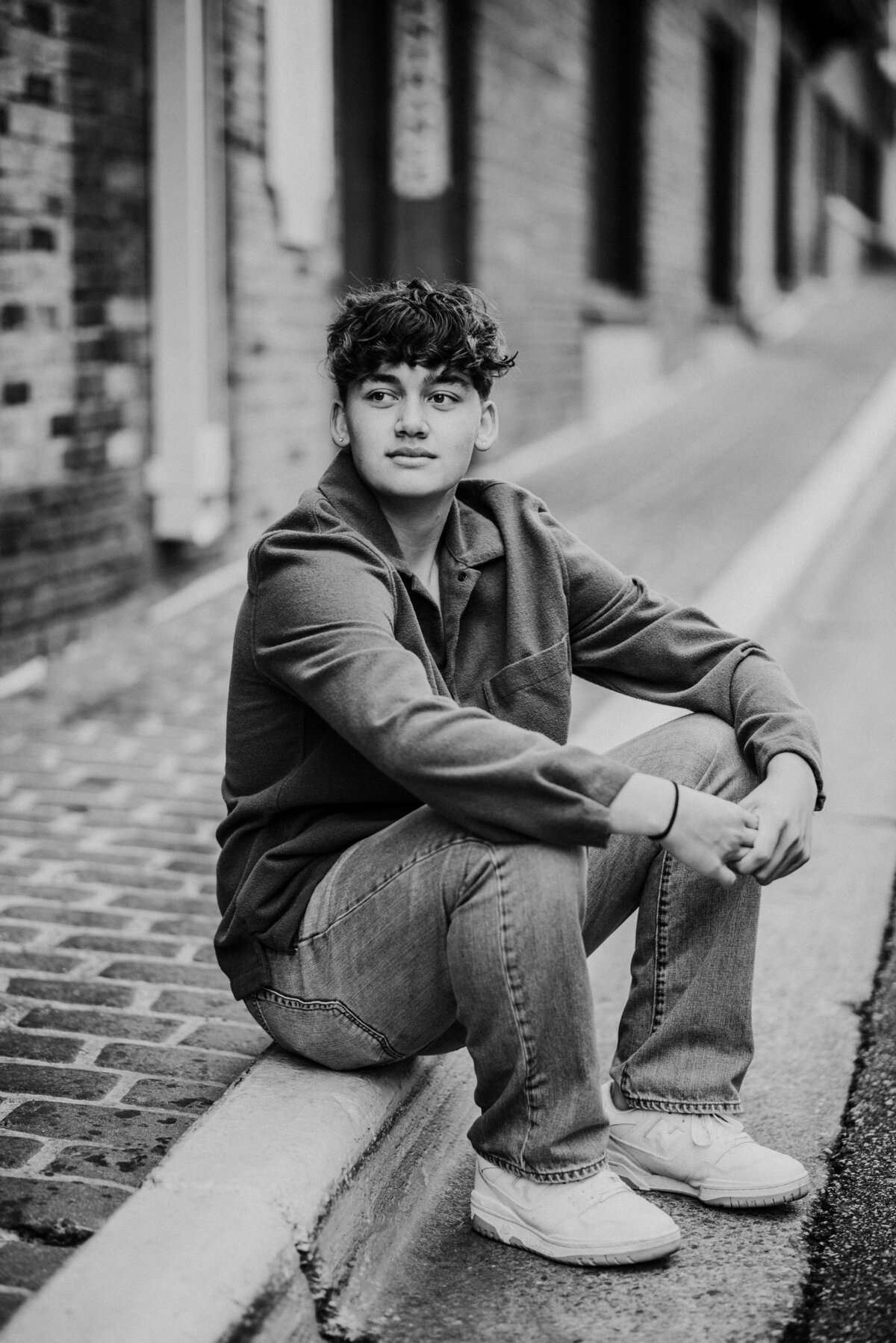 Amidst the charming streets of downtown Stillwater, another Stillwater High School graduate takes center stage in this senior portrait. Seated on a curb, he gazes wistfully into the distance, capturing the spirit of a young graduate ready to explore new horizons in the backdrop of a historic town.