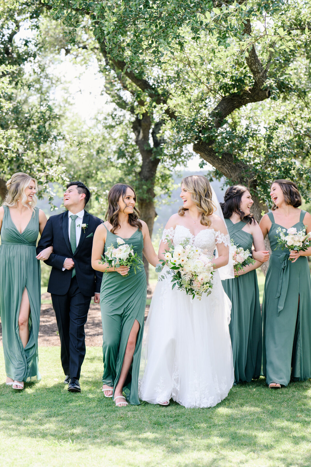 Bride walking with her bridal party in emerald green dresses under oak trees, planned with ease and style by a wedding planner in Austin.